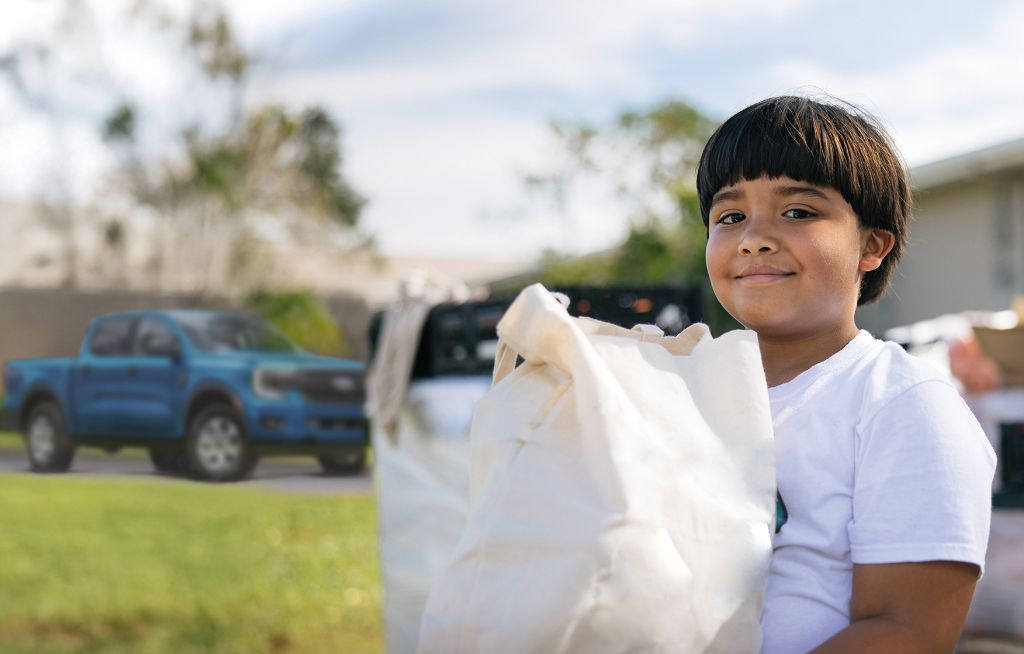 Campanha Setembro Solidário Ford Brasil Criança segurando uma sacola com picapes Ford de fundo