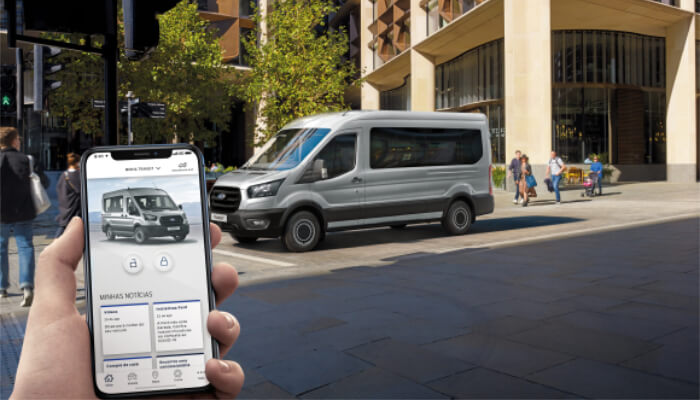 Ford Transit Minibus ao fundo e homem segurando celular com tela exibindo o aplicativo FordPass