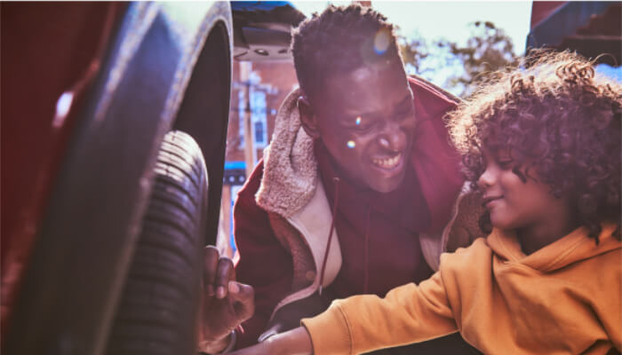 Homem e criança verificando a roda de um veículo e sorrindo