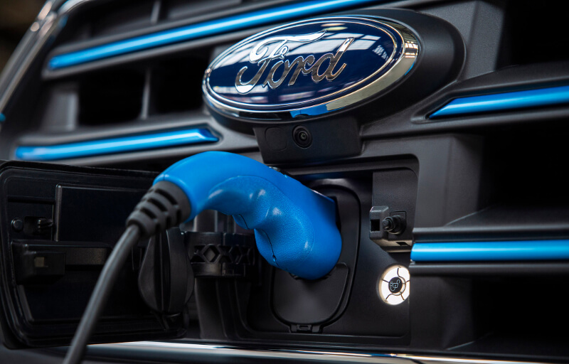 Detalhe do logo oval da Ford, com uma E-Transit acoplada ao carregador