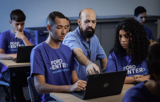 Instrutor orienta alunos em curso de tecnologia da Ford com uso de laptops.