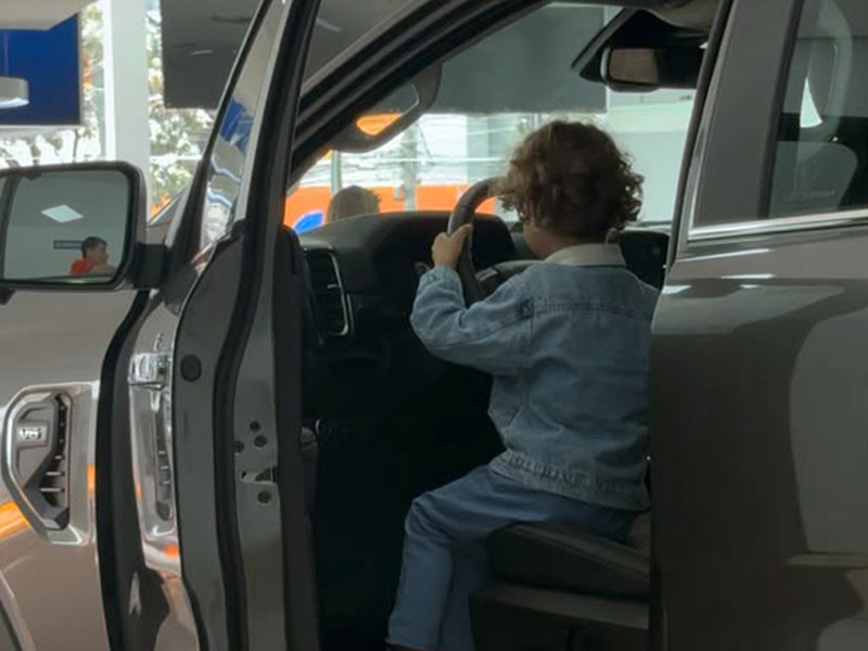 Criança Explorando o Interior de um Veículo Ford Criança sentada ao volante de uma picape Ford em uma concessionária