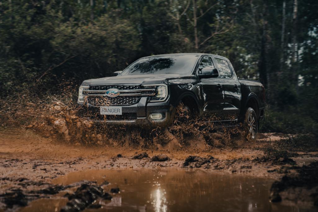 Ford Ranger XLT na cor preta em um terreno off-road, cercado por mata, trafegando por uma poça de lama