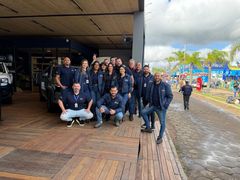 Equipe reunida na entrada do estande, com o parque de exposicoes ao fundo 