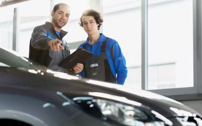 Dos trabajadores de taller revisando y señalando un automóvil