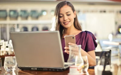 Mujer sentada en un restaurante revisando su laptop y su teléfono celular