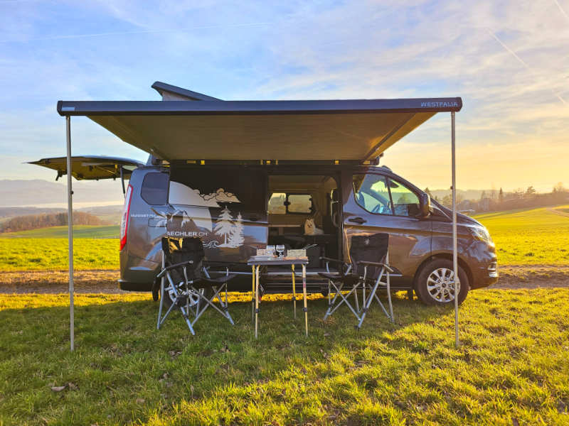 Schwarzer Camperwage steht auf Feld im Sonnenschein