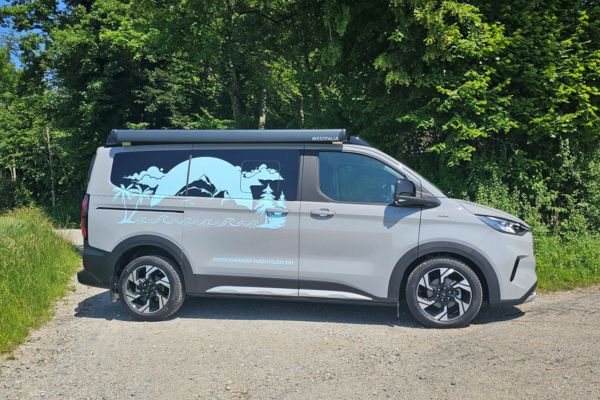 Transit Custom Nugget in grau parkt auf Strasse mit grünen Bäumen im Hintergrund