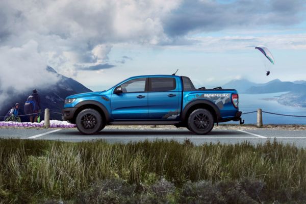 Ford Ranger Raptor in lau parkt auf Parkplatz und im Hintergrund fliegen Paraglider