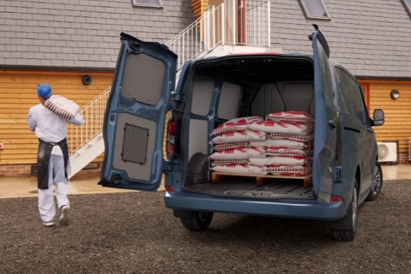 Ford Transit Custom steht mit offenem Laderaum vor Gebäude und Mann trägt Sack ins Innere