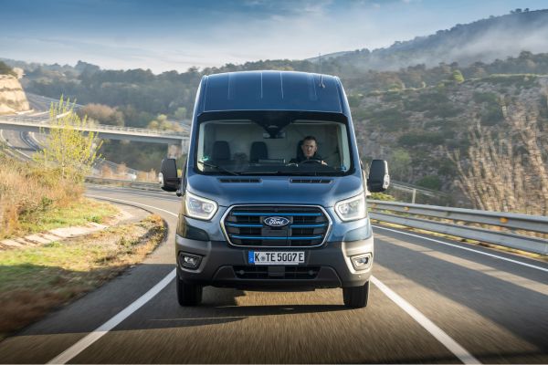 Ford E-Transit fährt auf Landstrasse mit weiten Felden im Hintergrund