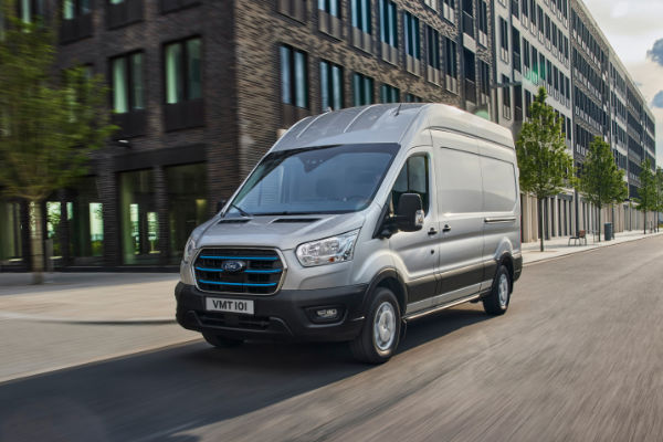 Ford E-Transit fährt durch Stadt vorbei ein Gebäuden mit Glaswänden