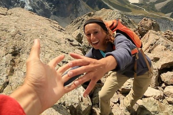 Lächelnde Frau streckt sich nach Hand auf Berg beim Wandern