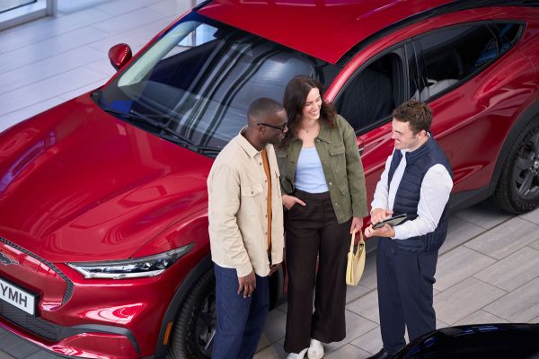 Ford Care Plus / Premium Mitarbeiter und zwei Kunden stehen vor rotem Ford-Fahrzeug
