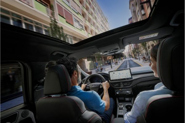 Zwei Personen sitzen in Ford-Fahrzeug und fahren durch Stadt