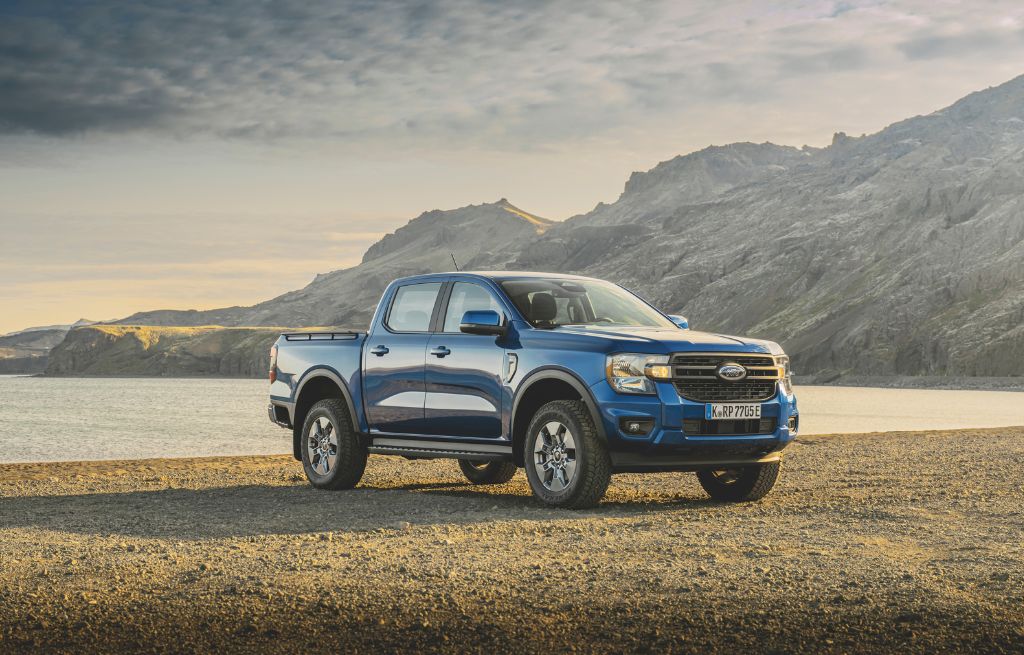 Blauer Ford Ranger am Ufer eines Sees, im Hintergrund schroffe Berge und dichte dunkle Wolken.