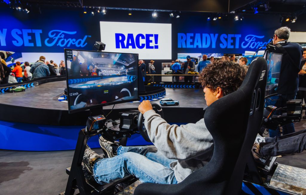 Ein Besucher spielt an einem virtuellen Rennsimulator auf einem modern beleuchteten Ford-Messestand