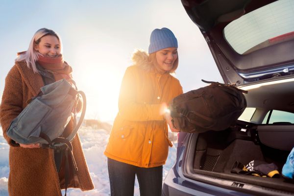 Wintercheck Eine lächelnde Frau lädt ihren Rucksack in den Kofferraum Ihres Ford, der in einer Winterlandschaft geparkt ist