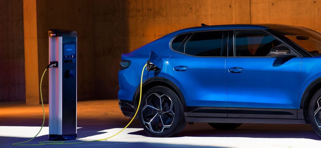 Une Ford Capri bleue devant une station de recharge sur fond orange
