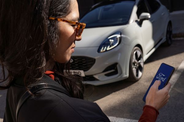 Une femme regarde l'application Ford devant une Ford Puma.