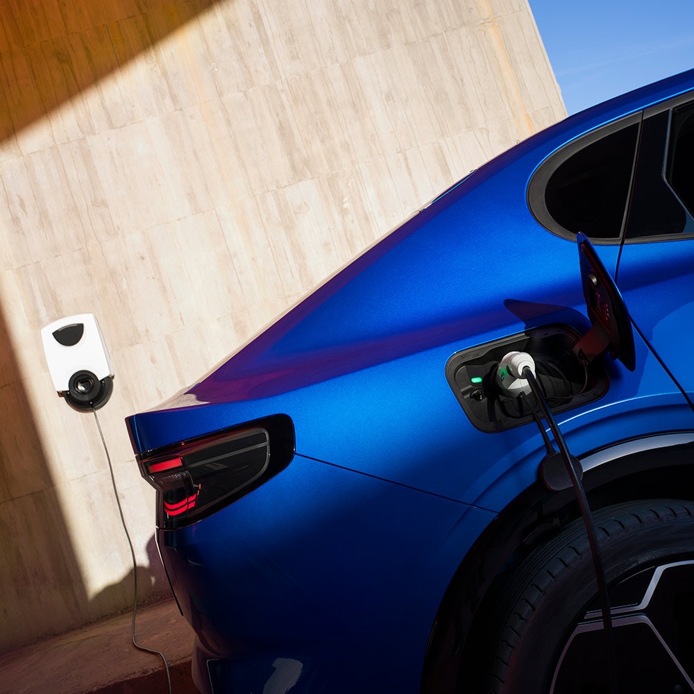 Vue arrière d'un véhicule électrique Ford Capri bleu branché à une borne de recharge domestique