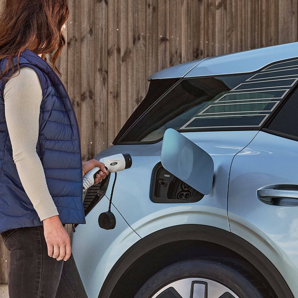 Une femme connectant un Ford Explorer électrique bleu à un chargeur domestique