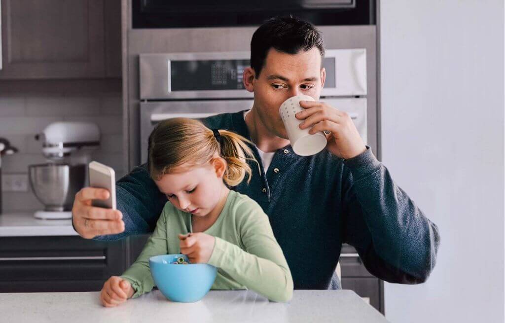 Homme avec un enfant consultant son téléphone portable en prenant leur petit-déjeuner