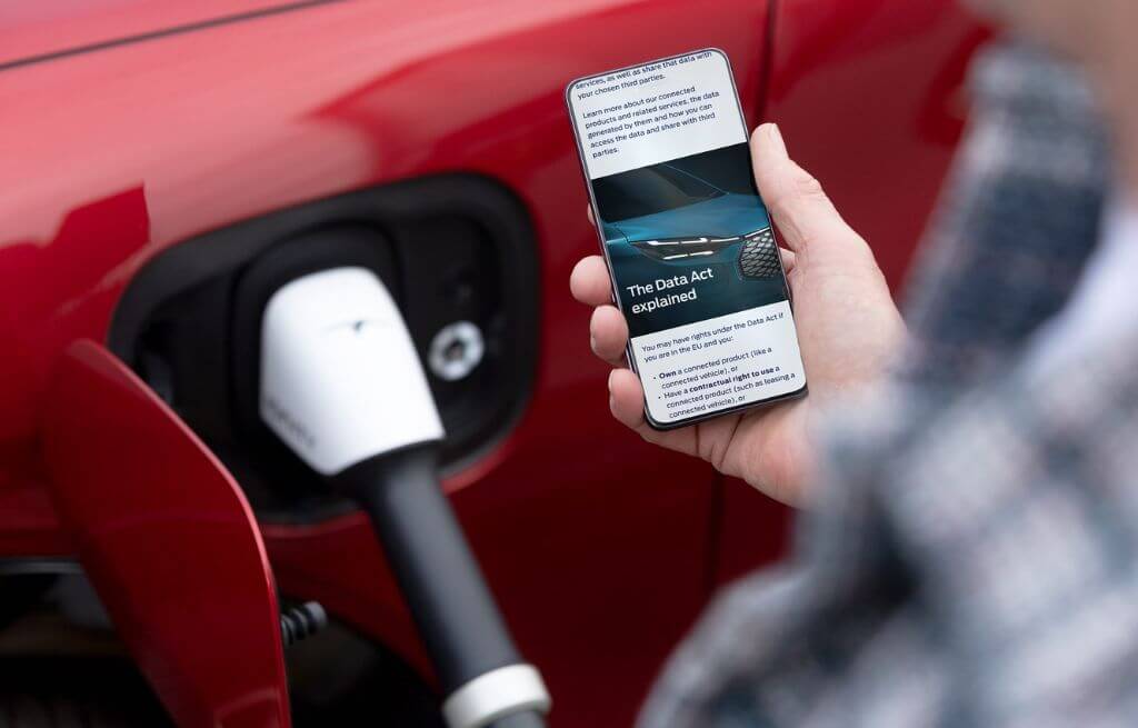 Une personne vérifiant son smartphone, un véhicule électrique rouge en charge en arrière-plan