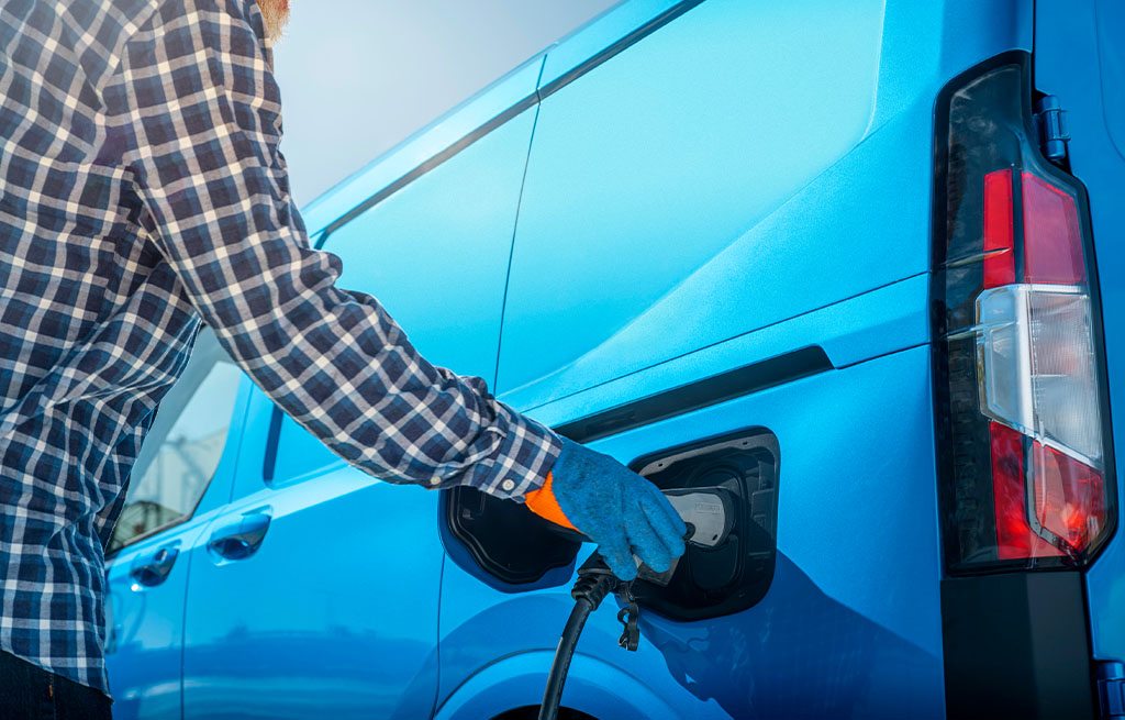 Person charging a blue electric cargo van at a charging station