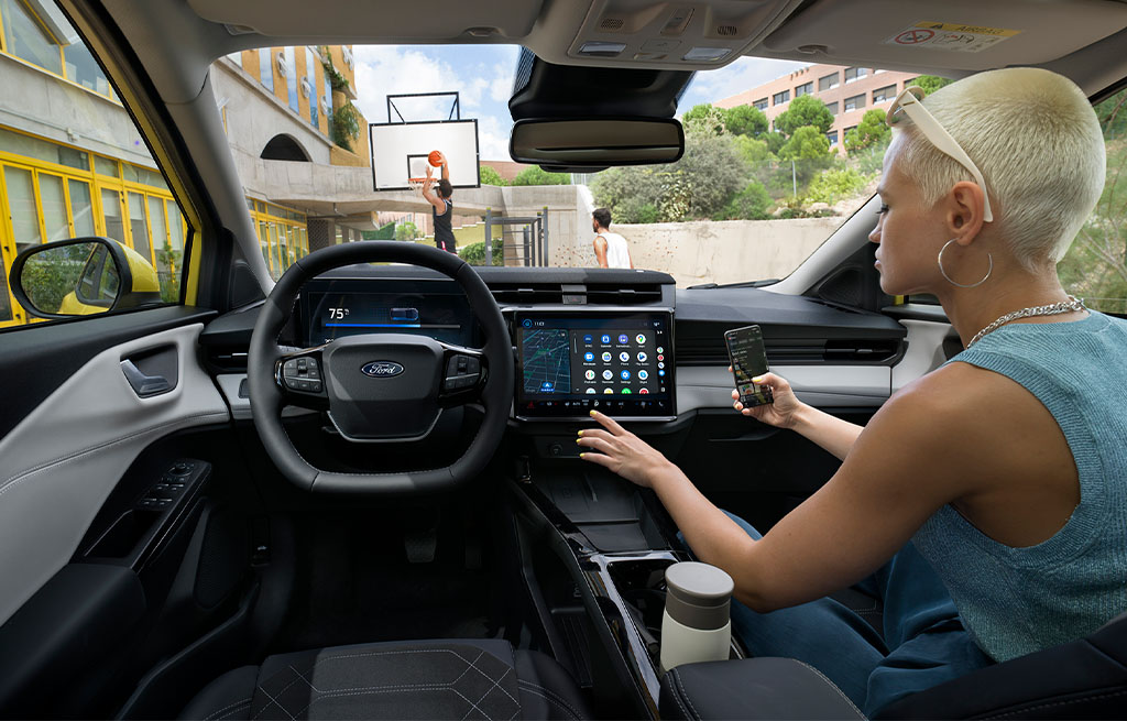 A woman with short blonde hair sits in the driver’s seat of a parked electric car