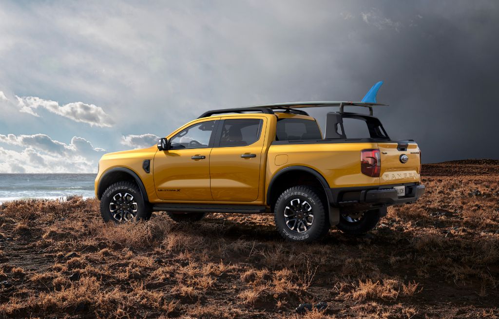 Gul Ford Ranger pickup med surfebrett på takstativ ved kysten