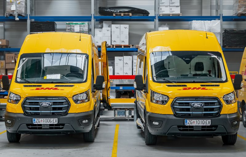 To gule DHL Ford Transit varebiler parkert på lager