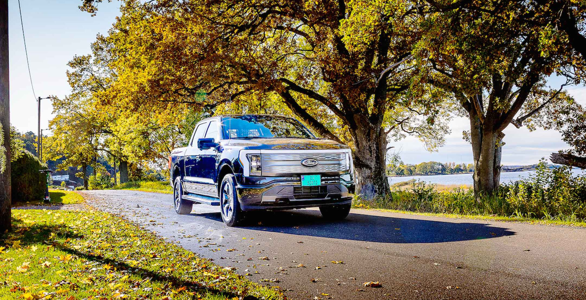 Blå Ford F-150 Lightning på vei ved siden av trær