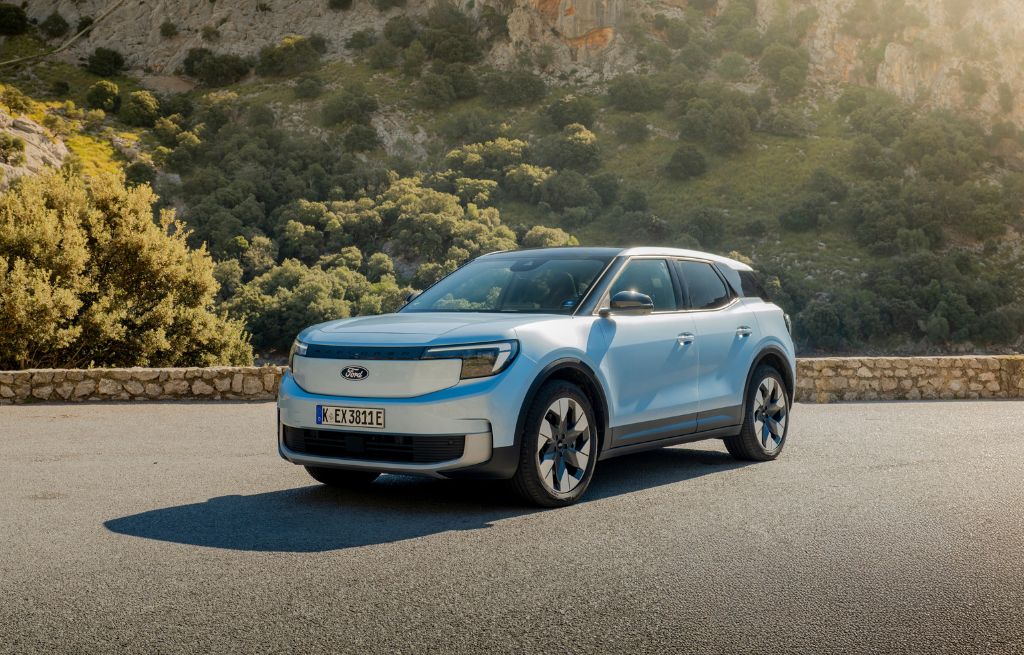 Ljusblå elektrisk SUV parkerad på en väg med berg och grönska i bakgrunden