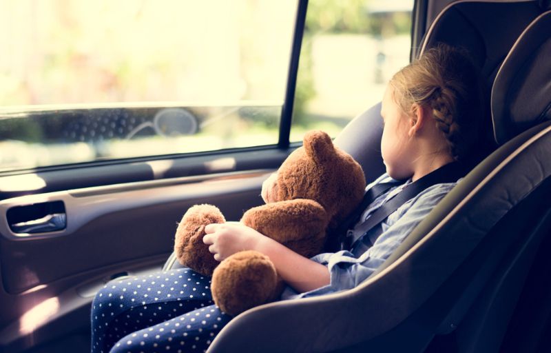 Barn som sitter säkert i en bilbarnstol och håller en nallebjörn i bilen